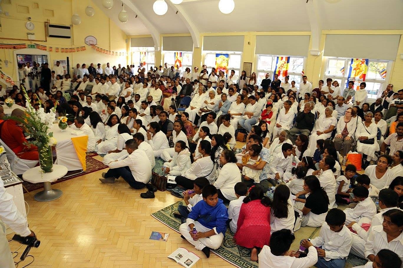 The community gathered in white for a ceremony at the Vihara, with Buddhist flags at the windows