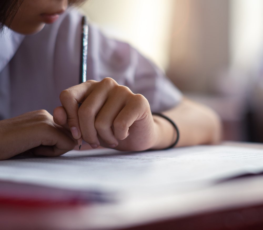 A pupil's hand holding a pencil over a written page at a desk