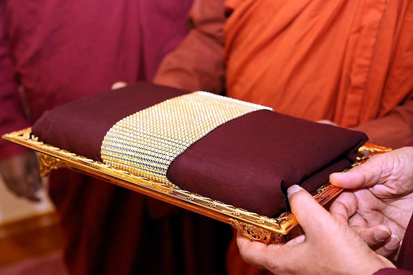 A folded robe presented on a gold tray during a robe-offering ceremony